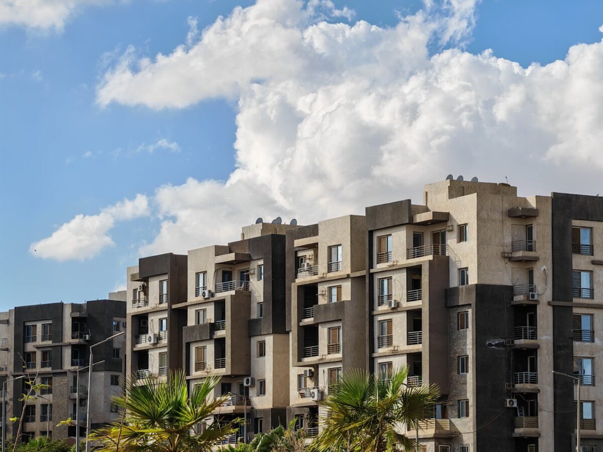 Contemporary urban apartment buildings under a bright blue sky with palm trees.