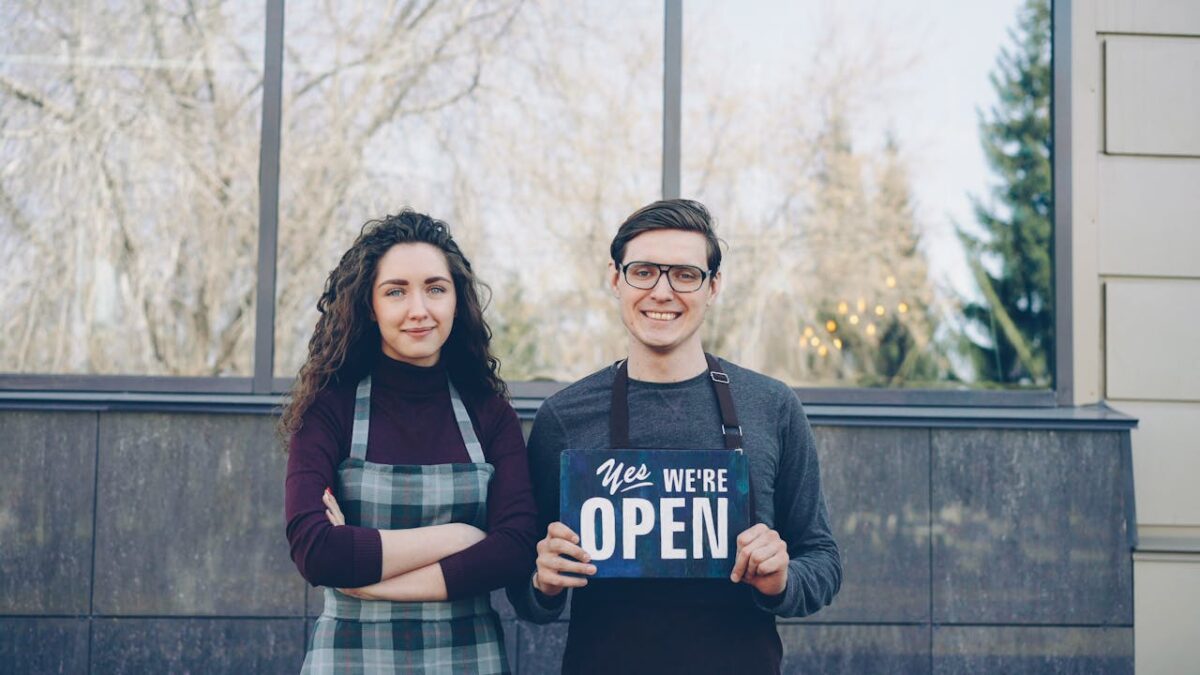 services-01 Two business owners standing outside, holding a 'Yes We're Open' sign, welcoming customers.