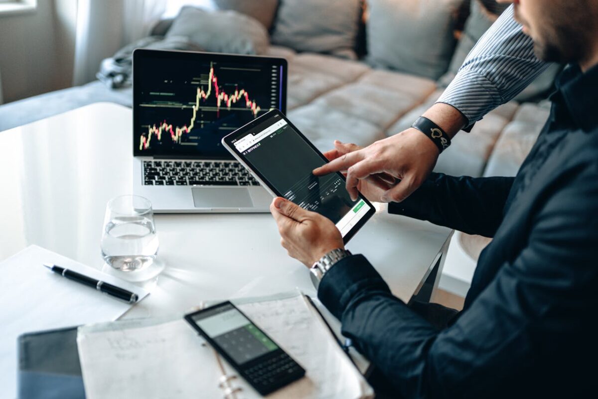 services-02 Professionals reviewing stock market trends on a tablet and laptop, discussing investment strategies.
