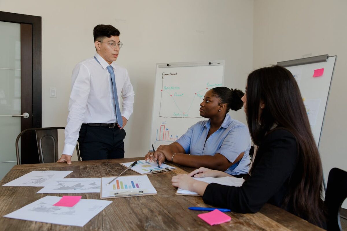 who-we-are A diverse group of professionals engaged in a meeting around a boardroom table.